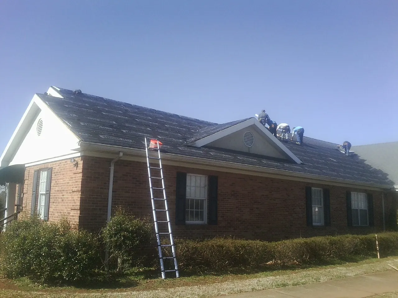 Crew tearing shingles off a brick ranch roof with a ladder set — Metal Roof Repair work by our crew in Ravenna