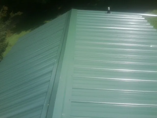 New green metal panels meeting at the ridge of a roof — Flat Roof Repair work by our crew in Ravenna
